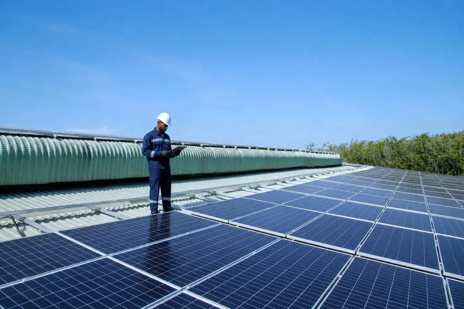 Solar technician in navy workwear checking a tablet while inspecting a rooftop solar installation